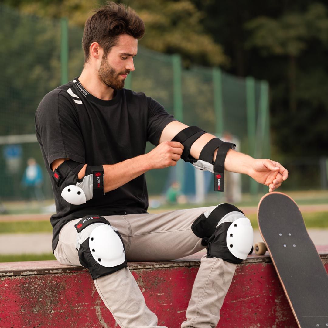 Skateboarder on a ledge strapping on black and white SKATEWIZ pads